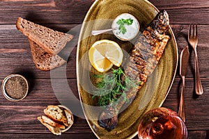 Baked fish with lemon and greens on plate on wooden background. Delicious dish of seafood.
