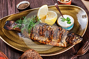 Baked fish with lemon and greens on plate on wooden background. Delicious dish of seafood.