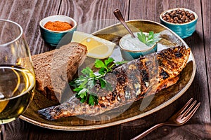 Baked fish with lemon and greens on plate on wooden background. Delicious dish of seafood