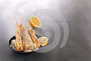 Baked fish on skewers in a black plate and french fries on a wooden table.