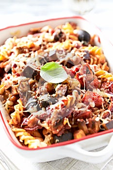 Baked fusilli pasta with cherry tomatoes, olives and mozzarella cheese. Bright wooden background.