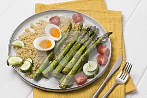 Baked green asparagus, bulgur, fresh tomatoes, cucumber and boiled eggs with herbs on a plate