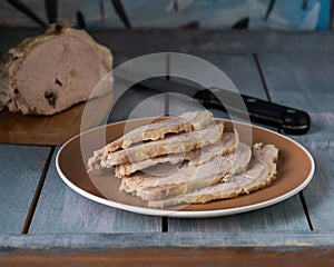 Baked ham, sliced on a round plate and a large piece of ham in the background lay on a wooden table