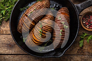 Baked hasselback sweet potato on cast iron pan. wooden background
