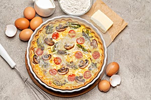 Baked homemade quiche pie in ceramic baking form, eggs and cream