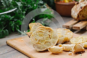 Baked knob of garlic on a wooden plate with cloves of garlic beside it.