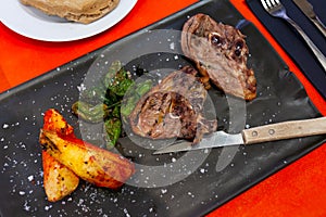 Baked lamb leg slices with potato wedges and padron peppers on slate board