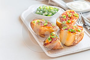 Baked loaded potato skins with cheddar cheese and bacon on a ceramic plate, garnished with scallions and sour cream, horizontal,