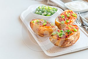 Baked loaded potato skins with cheddar cheese and bacon on ceramic plate, garnished with scallions and sour cream, horizontal, co