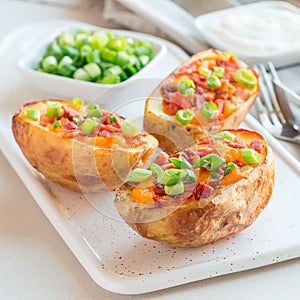 Baked loaded potato skins with cheddar cheese and bacon on a ceramic plate, garnished with scallions and sour cream, square format