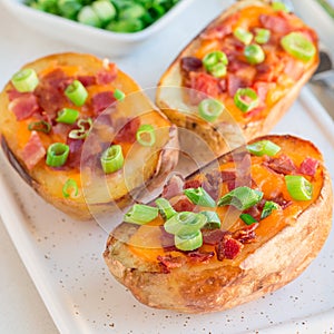 Baked loaded potato skins with cheddar cheese and bacon on ceramic plate, garnished with scallions and sour cream, square format