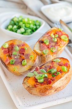 Baked loaded potato skins with cheddar cheese and bacon on ceramic plate, garnished with scallions and sour cream, vertical