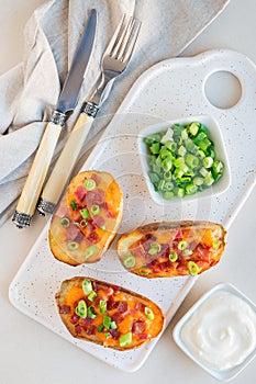Baked loaded potato skins with cheddar cheese and bacon on a ceramic plate, garnished with scallions and sour cream, vertical, top