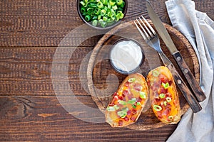 Baked loaded potato skins with cheddar cheese and bacon on wooden plate, garnished with scallions and sour cream, horizontal, top