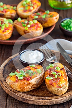 Baked loaded potato skins with cheddar cheese and bacon on wooden plate, garnished with scallions and sour cream, vertical