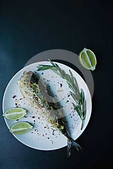 Baked mackerel served on a plate, decorated with spices, herbs and vegetables. Proper nutrition. View from above. Dark background
