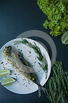 Baked mackerel served on a plate, decorated with spices, herbs and vegetables. Proper nutrition. View from above. Dark background