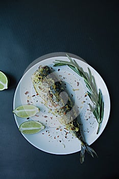 Baked mackerel served on a plate, decorated with spices, herbs and vegetables. Proper nutrition. View from above. Dark background
