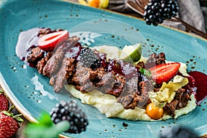 Baked meat with mashed potatoes and blackberry sauce in plate on wooden background. Healthy food, meat dishes, close up