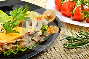 Baked meat stuffed with onion, mushrooms, cheese, parsley on black plate, tomatoes appetizer, rosemary