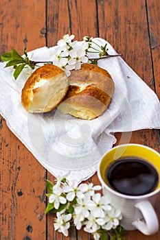 Baked open rolls and a cup of coffee on a dark, worn rustic wooden table. The composition is decorated with a twig with white