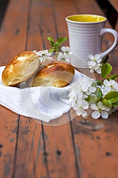 Baked open rolls and a cup of coffee on a dark, worn rustic wooden table. The composition is decorated with a twig with white