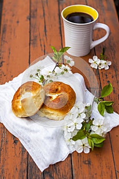 Baked open rolls and a cup of coffee on a dark, worn rustic wooden table. The composition is decorated with a twig with white