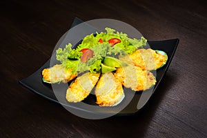 Baked oysters in cheese with lettuce and tomato in a black plate on the wooden brown table