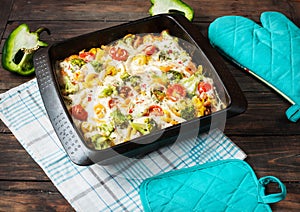 Baked pasta with broccoli and cheesy tomato sauce on wood background