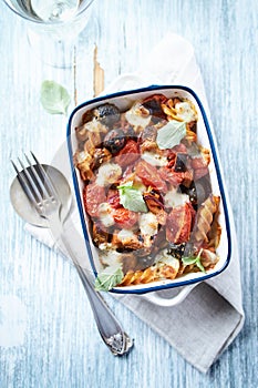 Baked pasta with cherry tomatoes, olives and mozzarella cheese. Bright wooden background.