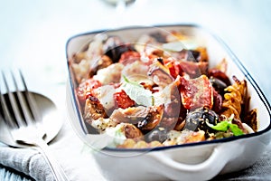 Baked pasta with cherry tomatoes, olives and mozzarella cheese. Bright wooden background.