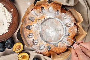 Baked plum pie dusted with powdered sugar, surrounded by raw ingredients, plum cake baking process