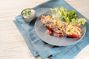 Baked pointed bell pepper stuffed with rice, tuna, tomatoes and cheese on a blue plate with lettuce salad, dip and parsley garnish