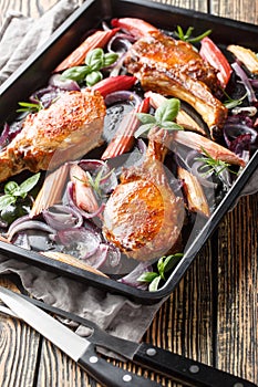 Baked pork chops with caramelized onions and rhubarb close-up in a baking sheet. Vertical