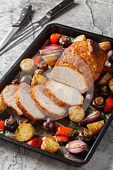 Baked pork loin with vegetables and mushrooms close-up on a baking sheet. Vertical