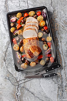 Baked pork loin with vegetables and mushrooms close-up on a baking sheet. Vertical top view