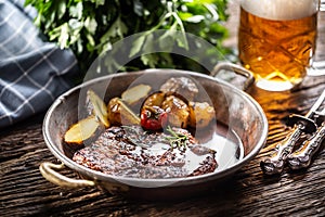 Baked pork nech with potaties served in metallic vintage bowl and beer photo