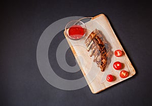 Baked pork ribs on cutting board on dark background. Top view, copy space