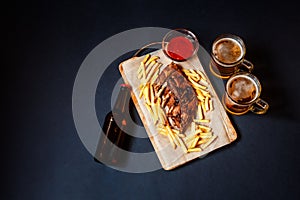 Baked pork ribs with french fries on cutting board and beer. Top view, copy space