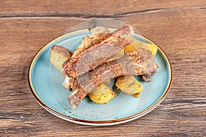Baked pork ribs with potatoes in a plate on a wooden countertop.