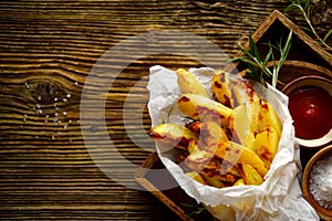 Baked potato fries, wedges with addition sea salt and rosemary on a wooden background, top view.