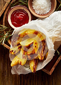 Baked potato fries, wedges with addition sea salt and rosemary on a wooden background, top view.