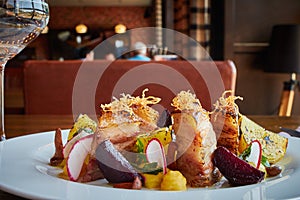 Baked potato slices and beets with vegetables and roast pork bacon on dark wooden table served in restaurant interior