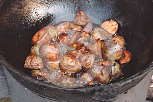 Baked potatoes cooked in yard cauldron with firewood burning in it, with lots of boiling sunflower oil