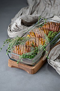 Baked potatoes with thyme in a glass container on a gray stone table