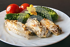 Baked poultry chicken wings, fresh tomatoes and green cucumbers on a white plate on a black background. Healthy healthy food for d