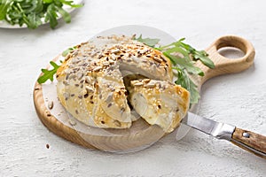 Baked in puff pastry cheese sprinkled with seeds decorated with fresh arugula leaves on a wooden board on a gray