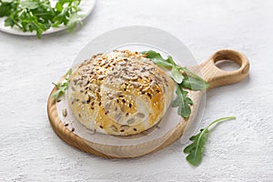 Baked in puff pastry cheese sprinkled with seeds decorated with fresh arugula leaves on a wooden board on a gray