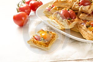 Baked puff pastry snacks with cream cheese, tomatoes and herb pesto, party finger food served on a white napkin and a plate at a