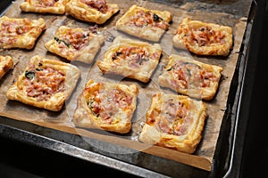 Baked puff pastry squares with ham, spinach and cheese on a tray with baking paper, finger food snack for a warm or cold party